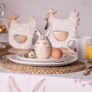 Een decoratief beeldje van een paasei, met op de achtergrond twee hanenbeeldjes, volledig in de sfeer van Pasen.