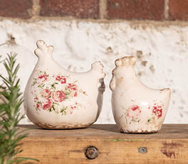 A collection of decorative objects adorns a windowsill. There are a total of seven items, all seemingly crafted from wood with different designs. They are placed on small pedestals, resembling trophies or decorative finials. The colors are predominantly earthy tones, with variations of brown and gray, giving off a rustic and antique feel. Alongside these wooden objects are two candle holders with intricate carvings that allow light to pass through in a charming manner. Behind these objects sits a potted houseplant, adding a touch of green to the scene and providing a refreshing contrast to the predominantly brown hues. The natural light streaming through the window imparts a warm and inviting ambiance to the entire arrangement.