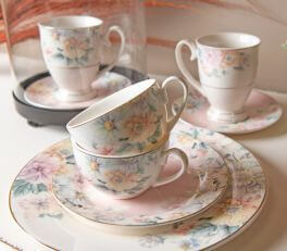 An elegant dinnerware set adorned with delicate floral designs graces the scene. We see three teacups accompanied by matching saucers and one plate, all seemingly crafted from fine porcelain. Each piece features graceful floral prints with a blend of pastel colors—predominantly pink, blue, and green—evoking a spring-like ambiance.

The teacups boast a classic shape with handles designed for easy grip. The flowers appear to be wildflowers or garden blooms, exuding a soft and romantic style.

The arrangement suggests that this set is intended for a traditional tea experience, perhaps in a serene, homely setting. The soft focus and natural light imbue the image with a warm, inviting atmosphere. The overall impression exudes a sense of tranquility and refinement, perfect for a peaceful tea moment.