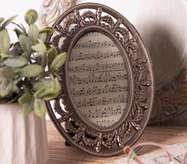 Two photo frames sit on a wooden surface, likely a part of a domestic interior. The left frame boasts a soft blue color with decorative bird and floral details in relief on the sides. Inside, there appears to be a small artwork or printed image featuring yellow flowering plants. The right frame is larger, sporting a classic white finish with intricate, floral-like patterns in relief at the corners and along the edges. It showcases an image or artwork with a delicate floral design, harmonizing with the nature-themed motif of the smaller frame.

Behind the frames, we partially see a woven object, possibly a basket or wall decoration, and on the right side, there is a piece of rope tied in a simple bow. Flanking the frames on both sides are green houseplants in terracotta pots, further enhancing the natural and rustic ambiance of the composition. The soft colors and use of natural materials and motifs suggest an appreciation for nature and a cozy, soothing atmosphere.