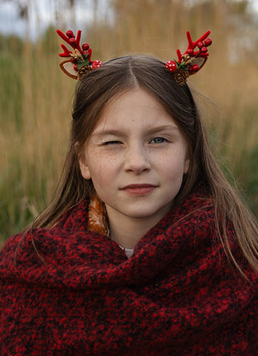 Une fille aux longs cheveux blonds ondulés, vue de la nuque vers le haut. Elle porte un large chapeau de paille beige orné d'un ruban élégant avec des plumes et des perles. Le chapeau jette une douce ombre sur son visage, le rendant partiellement visible. Elle tient un sac en jean, avec des détails de petites fleurs légères. L'ensemble dégage un style bohème et estival, et la fille semble poser contre un fond rustique de briques blanches, créant une atmosphère détendue et à la mode.