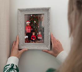 Two photo frames sit on a wooden surface, likely a part of a domestic interior. The left frame boasts a soft blue color with decorative bird and floral details in relief on the sides. Inside, there appears to be a small artwork or printed image featuring yellow flowering plants. The right frame is larger, sporting a classic white finish with intricate, floral-like patterns in relief at the corners and along the edges. It showcases an image or artwork with a delicate floral design, harmonizing with the nature-themed motif of the smaller frame.

Behind the frames, we partially see a woven object, possibly a basket or wall decoration, and on the right side, there is a piece of rope tied in a simple bow. Flanking the frames on both sides are green houseplants in terracotta pots, further enhancing the natural and rustic ambiance of the composition. The soft colors and use of natural materials and motifs suggest an appreciation for nature and a cozy, soothing atmosphere.