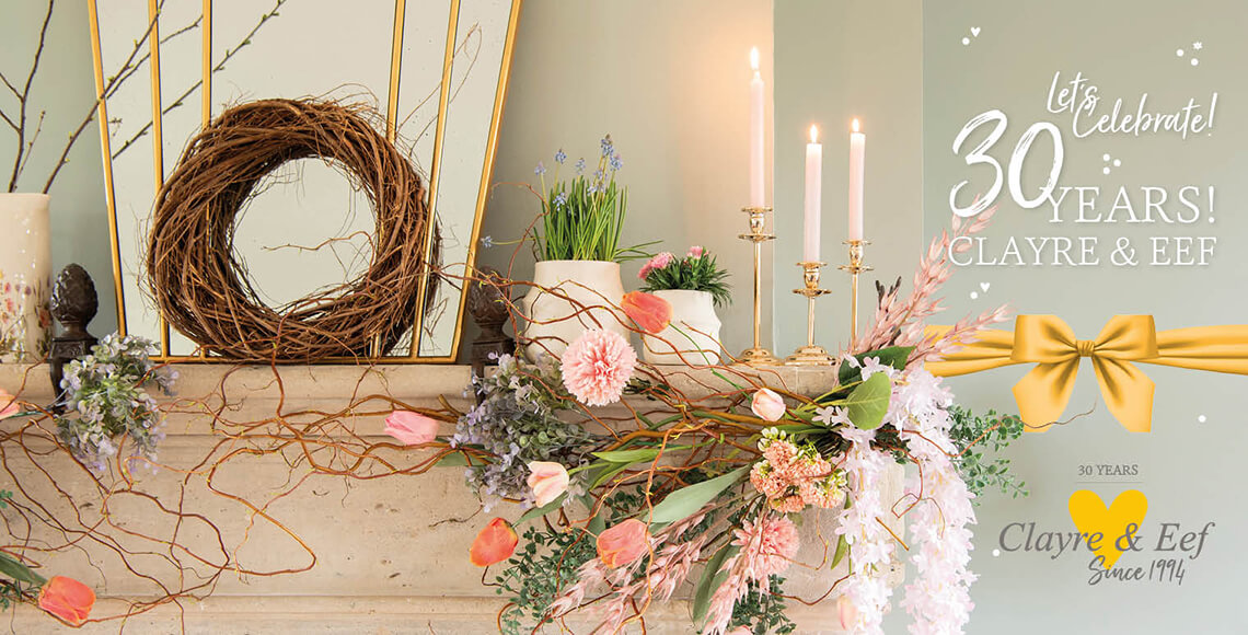A festive decoration celebrating Clayre & Eef's 30th anniversary. Central to the composition is a stylish fireplace adorned with a lavish arrangement of flowers and plants, including pink tulips and soft blossoms, collectively exuding a spring-like atmosphere. A natural wreath of branches hangs against the mirror, adding to the rustic and homely theme. Scattered across the mantelpiece are elegant candles in golden candlesticks, casting a warm glow on the surroundings. The scene is adorned with a large, golden ribbon with a bow, and the words "Let's Celebrate! 30 Years! CLAYRE & EEF" are prominently displayed in graceful white letters at the top of the image, creating an inviting and festive ambiance. The overall image is one of elegance and celebration, fitting for a special milestone.