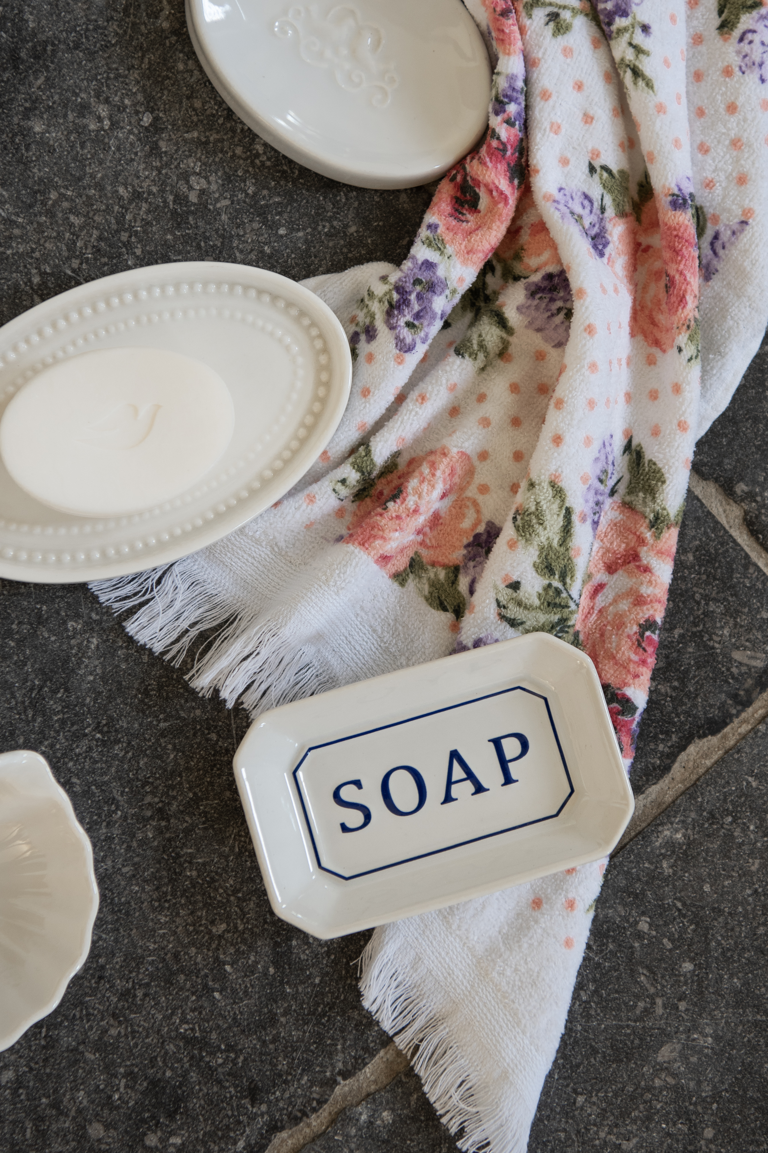 Two white ceramic soap dishes lying on the tiled floor with a guest towel