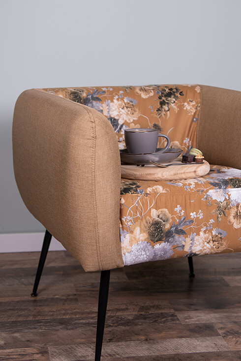 Ein beiger Stuhl mit Blumenmuster, auf dem ein hölzernes Tablett mit einer grauen Teetasse steht