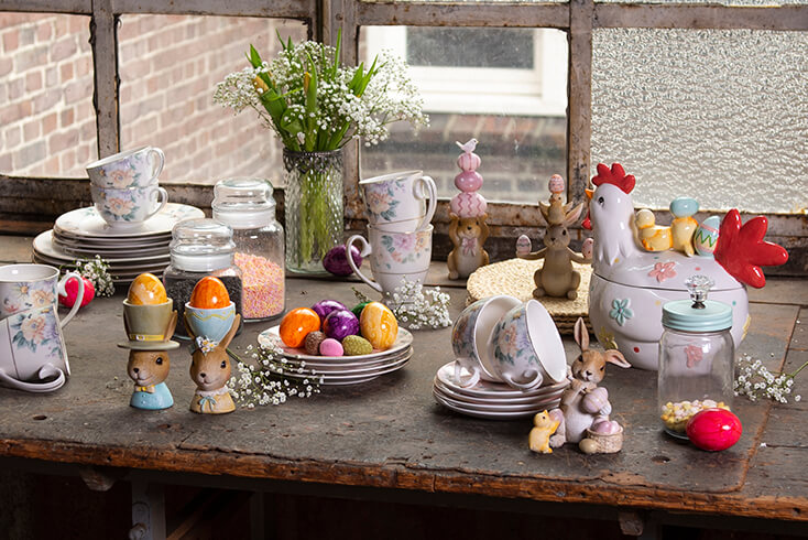 Een tafel gedekt voor pasen met paasservies, paashazen, kop en schotels, gekleurde eieren en eierdopjes
