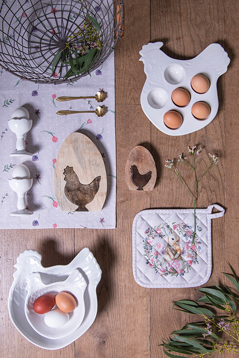Twee keramieken eierhouders met twee houten kippen beelden, een eierschaal in de vorm van een kip en een pannenlap voor pasen