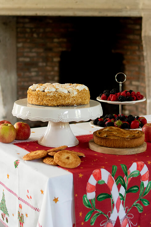 A rustic cake stand with cake and a Christmas tablecloth