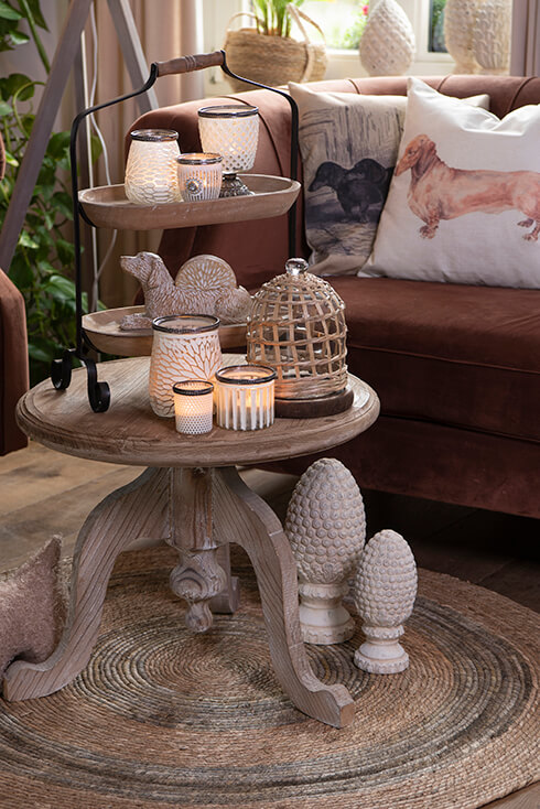 Une table d'appoint en bois avec trois porte-bougies, une cloche en verre et un étagère en bois avec des porte-bougies et un porte-sous-verres
