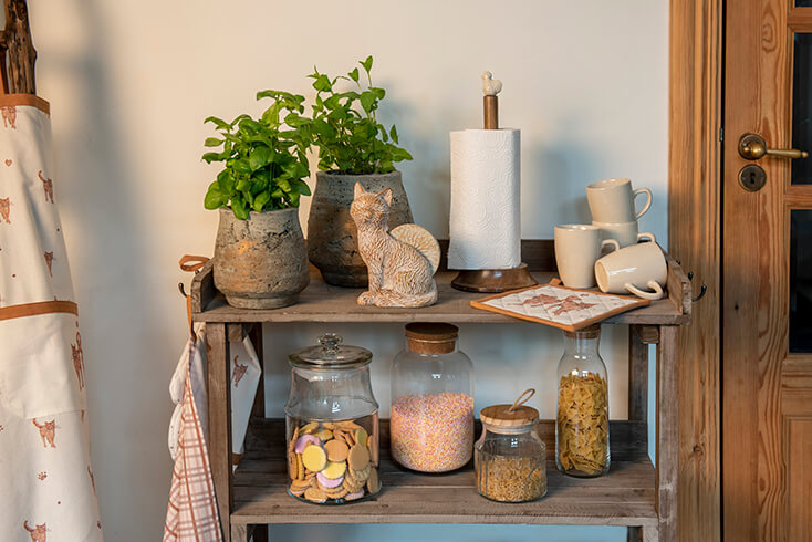 A rustic cabinet with glass storage jars, rustic flower pots, coaster holder, beige mugs, and a rustic kitchen roll holder