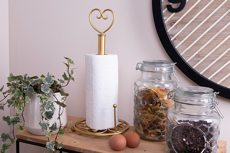 A gold-colored metal kitchen roll holder with a heart