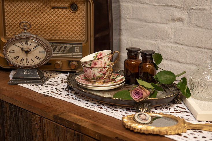 Eine Vintage-Dekoration mit einer rosa Rose, zwei Tassen und Untertassen, zwei Vasen, einem Tablett, einer Tischuhr und einem antiken Radio