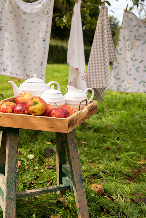 A wooden tray filled with apples and a tea pot and milk and sugar set