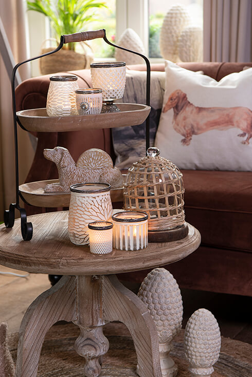 Une table d'appoint en bois avec une étagère en bois avec une cloche en verre, des porte-bougies et un chien en bois avec des dessous de verre
