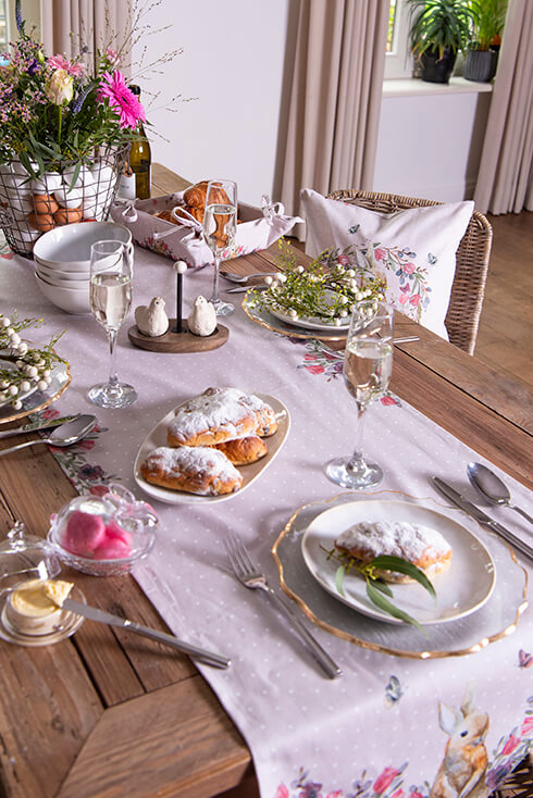 Een gedekte paastafel met servies, paasbrood, wijnglazen, roze tafelloper, keramieken peper- en zoutstel