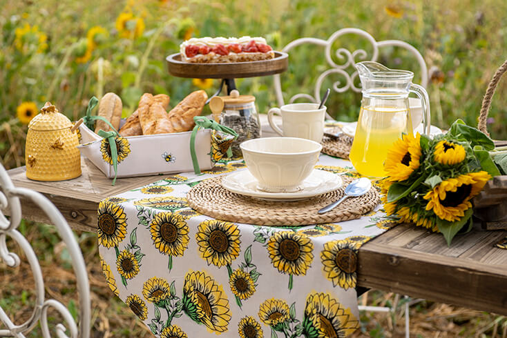 Een wit zonnenbloem tafelkleed, een broodmandje, een placemat, een schenkkan, servies en bestek