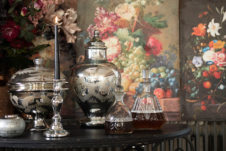 Ein silberner Kerzenständer mit einer schwarzen Abendkerze und silbernen Vasen und eine Glas-Karaffe