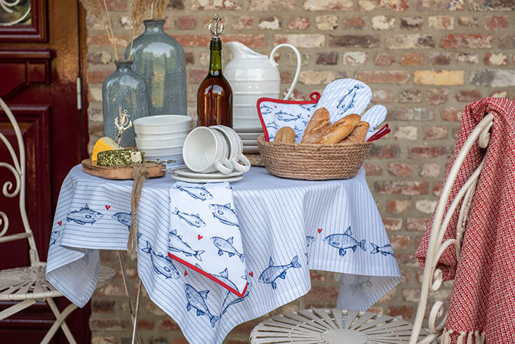 A maritime tablecloth with fish, vases, a bread basket, dishes, and a breadboard