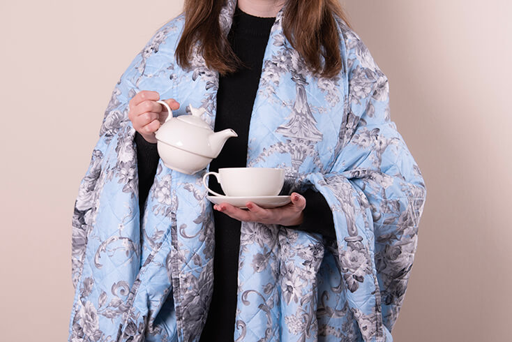 Een persoon die een tea for one inschenkt met een blauwe bedsprei omgeslagen