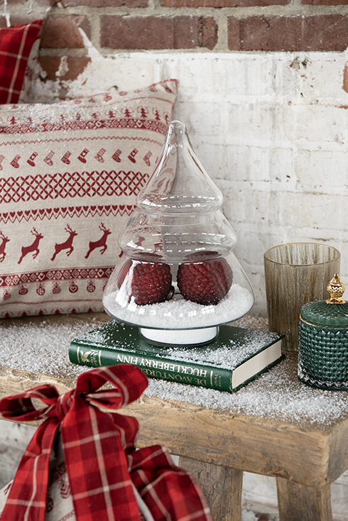 Un bocal en verre en forme de sapin de Noël avec de la fausse neige et deux boules de Noël rouges