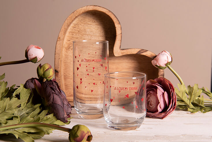 Two drinking glasses with red hearts and a wooden heart-shaped dish
