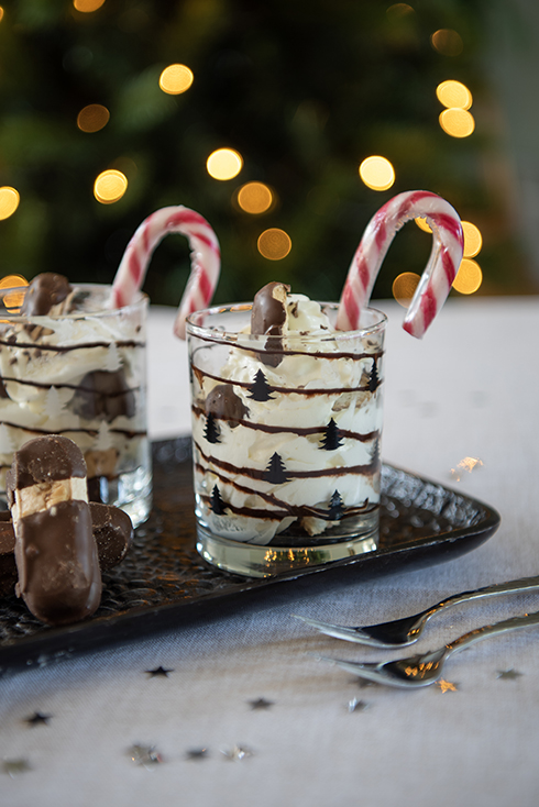 A drinking glass filled with black Christmas trees topped with whipped cream and candy canes