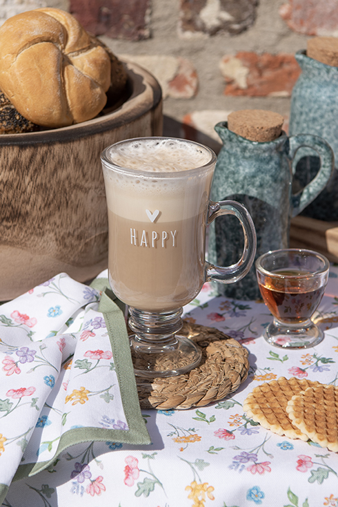 A tea glass with a latte macchiato on a wicker coaster