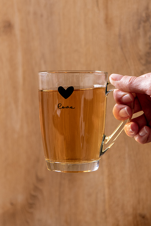 A tea glass filled with tea with the word "love" and a black drawn heart