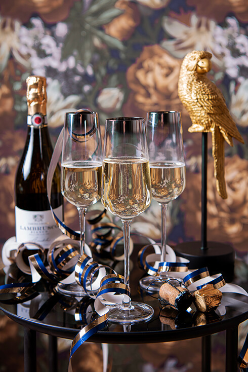 Three New Year's wine glasses with a champagne bottle and a gold parrot in the background