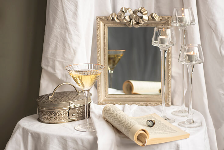 A martini glass with a silver box, three glass candleholders, and a gold mirror