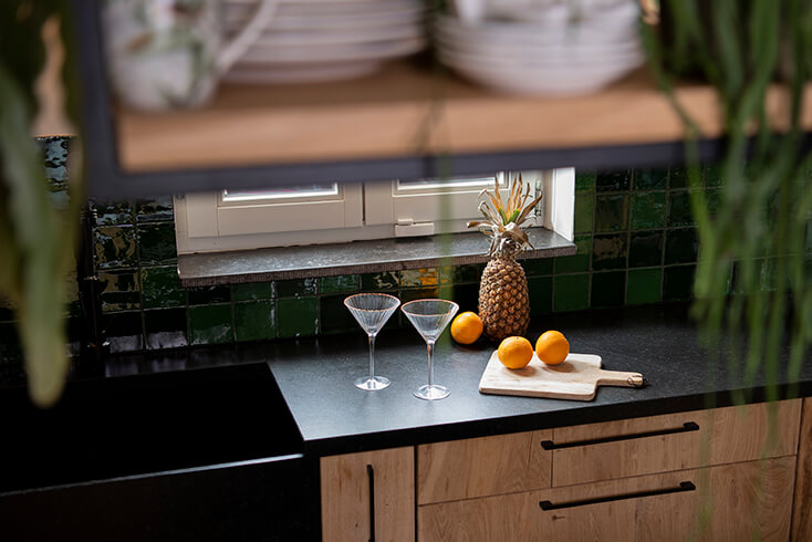 Two martini glasses, a wooden cutting board, pineapples, and mandarins on a black countertop
