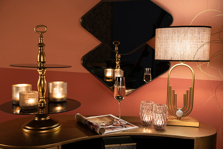 Un étagère dorée avec des porte-bougies, un verre à vin et une lampe de table