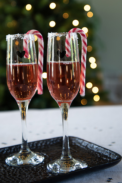 Two champagne glasses with a candy cane on the rim