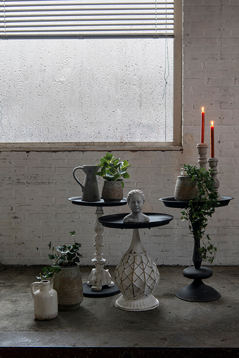 Trois tables d'appoint blanches et noires avec des pots de fleurs, des porte-bougies, des figurines et des pichets
