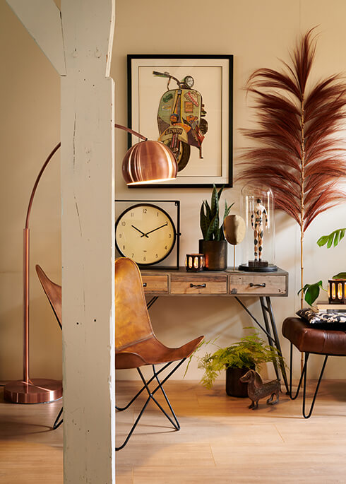 Una scrivania in legno con una sedia in pelle marrone e una lampada da terra in rame, un quadro, un orologio da tavolo e accessori per la casa decorativi