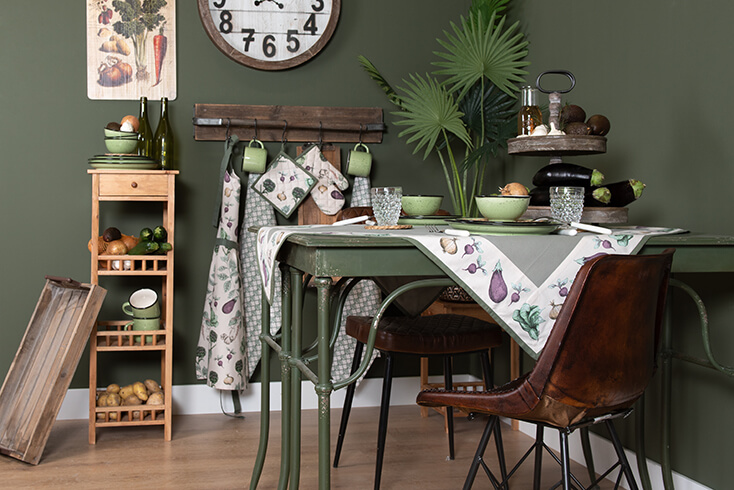 Une cuisine campagnarde avec une table à manger verte, des chaises de salle à manger marron, des accessoires de cuisine décoratifs et du textile de cuisine