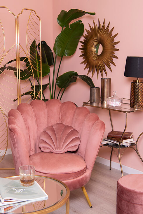 Un fauteuil rose avec un coussin rose, et derrière lui, un paravent doré et un miroir mural doré