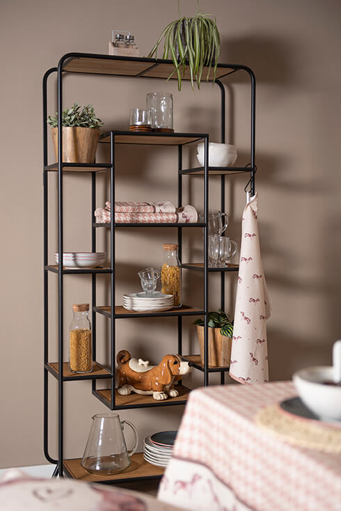 Een industriële boekenkast met allerlei decoratieve objecten, zoals een theedoek, bloempot, servies, voorraadpot en servetten