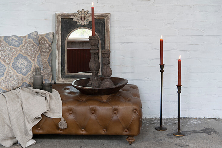 Ein Ledershocker mit einem Holztablett und zwei Kerzenständern, und an der Wand gibt es einen Spiegel