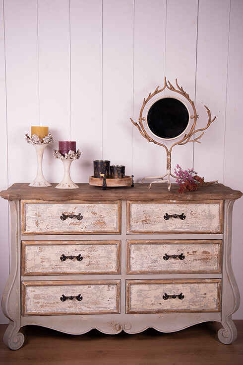 Una cassettiera rustica con uno specchio da tavolo, due portacandele e portatealight su un vassoio di legno