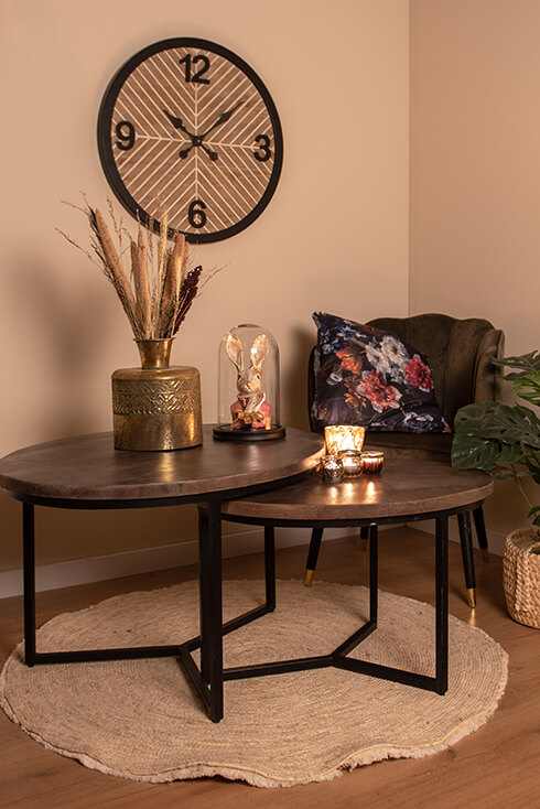 Deux tables basses avec un vase doré rempli de fleurs séchées, une cloche avec une figurine de lapin et une collection de photophores