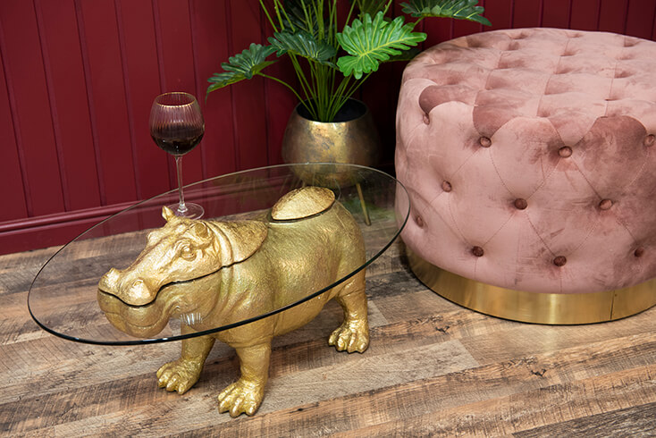 Une table basse en forme d'hippopotame avec un verre à vin, à côté se trouve un pouf rose