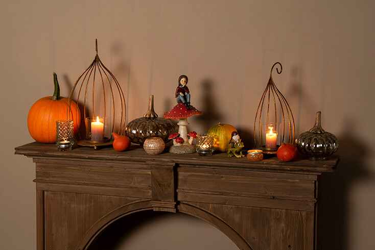 A brown fireplace mantel decorated with autumn decor, including sculptures, pumpkins, lanterns, and tea light holders