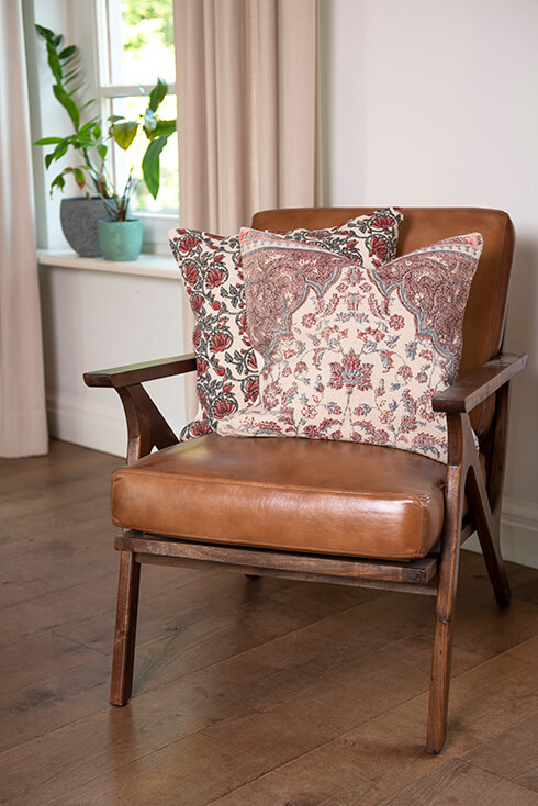 Un fauteuil en cuir vintage avec deux coussins botaniques
