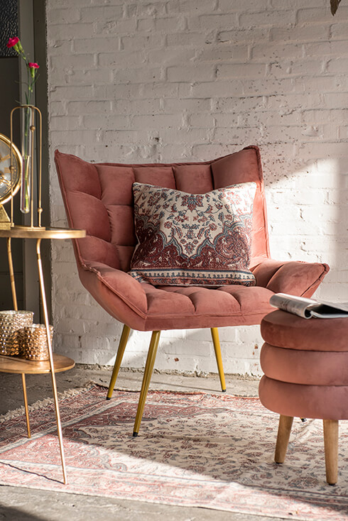 Ein rosa Sessel mit einem rosa Hocker, einem großen Teppich und einem goldfarbenen Beistelltisch und einer Stehlampe