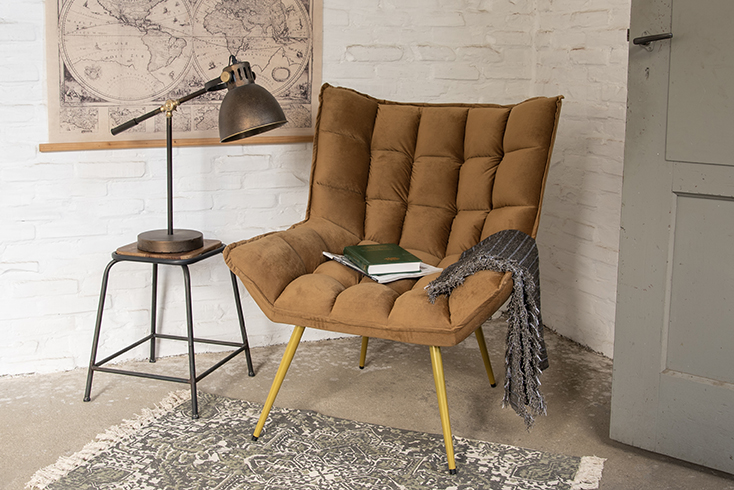 Ein industrieller Stil mit einem braunen Sessel, einer Decke, einem großen Teppich und einem Hocker mit einer industriellen Tischlampe