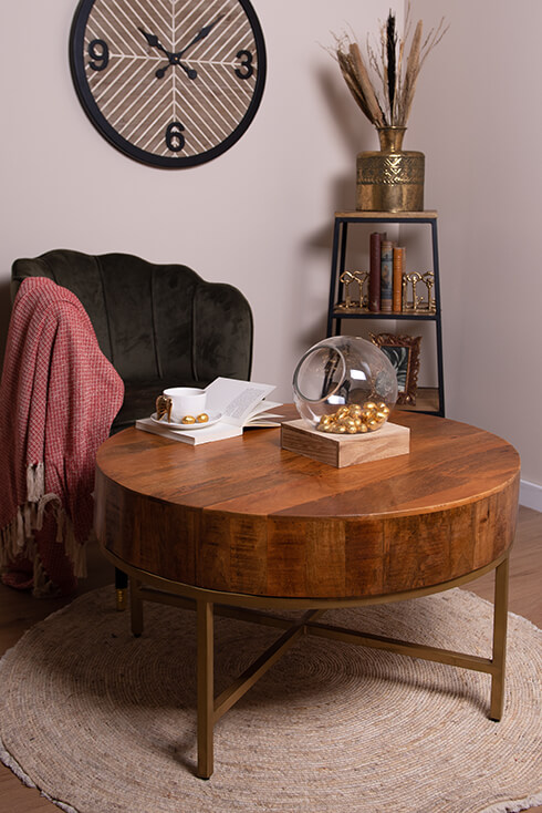 A wooden coffee table with a vase, a cup and saucer, and a book, and behind it, there's a chair with a throw blanket draped over it