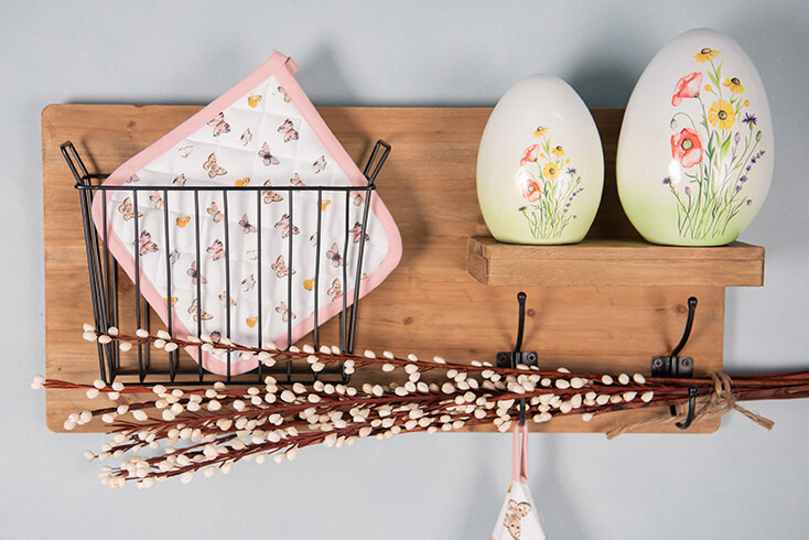 Una mensola da parete in legno con due uova decorative e una presina con farfalle