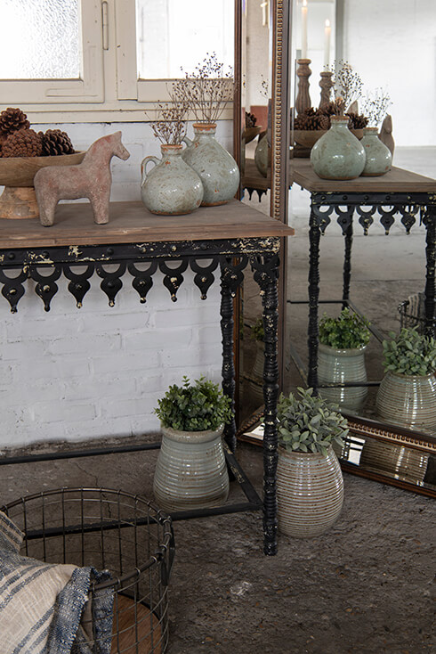 Une console rustique avec une statue de cheval, un présentoir à gâteaux et deux vases, à côté se trouve un miroir sur pied rustique avec deux pots de fleurs
