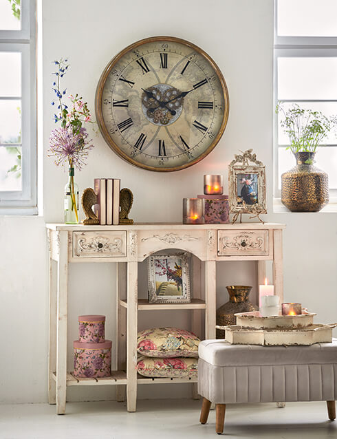 Un style d'intérieur shabby chic avec une console blanche remplie de décoration d'intérieur, et une grande horloge est accrochée au mur